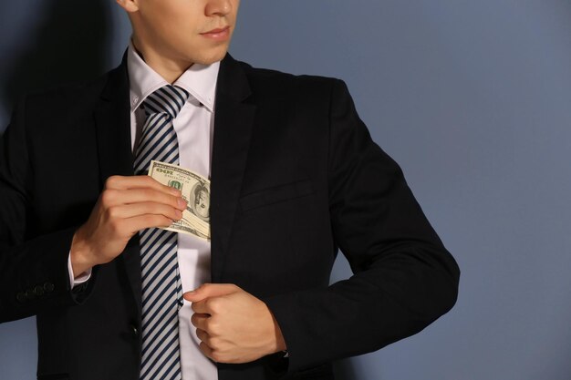 Attraktiver Mann, der Dollarnoten im Anzug auf grauem Hintergrund versteckt