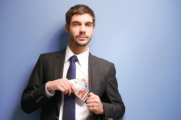 Attraktiver Mann, der Euro-Banknoten im Anzug auf Blau versteckt