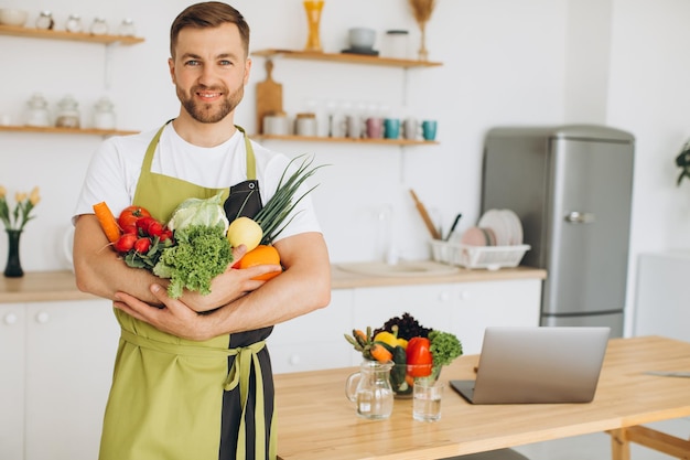 Attraktiver Mann, der zu Hause viele verschiedene frische Gemüsesorten in der Küche hält