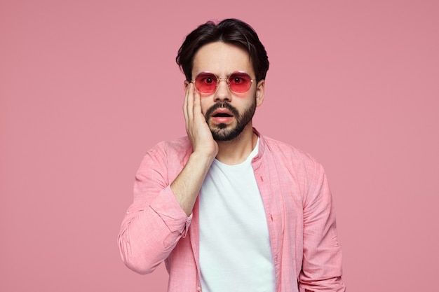 Attraktiver Mann in rosa Hemd und Sonnenbrille erstaunt über rosa Wand