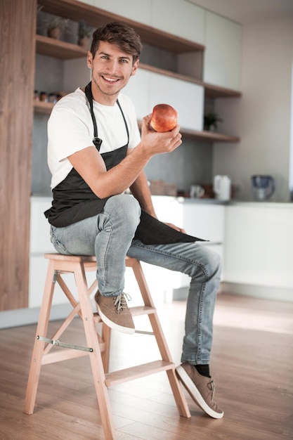 Attraktiver Mann mit einem Apfel, der in einer Hauptküche sitzt