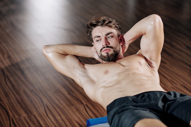 Attraktiver muskulöser bärtiger junger Mann, der Sit-ups auf Bank im Fitnessstudio tut