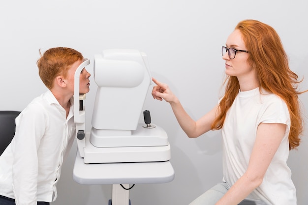 Foto attraktiver weiblicher augenarzt, der jungenaugen mit refraktometermaschine an der optikklinik überprüft