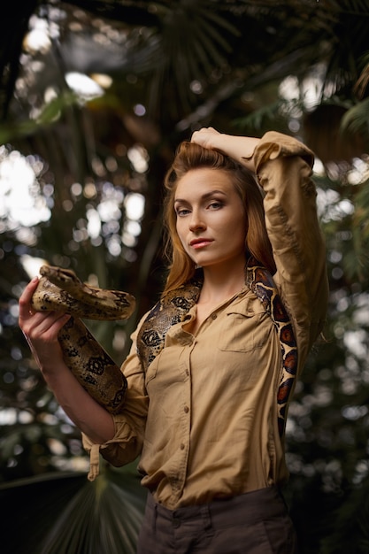 Attraktiver weiblicher Tierpfleger mit Pythonschlange in tropischer Natur