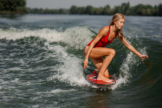 Attraktives blondes Mädchen, das auf dem roten Wakeboard reitet