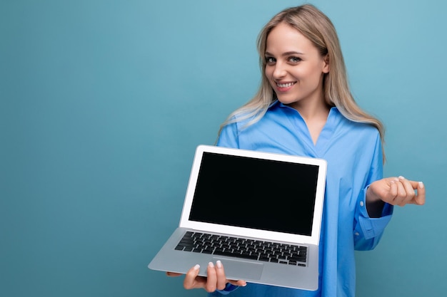 Attraktives blondes Mädchen mit leerem Bildschirm eines tragbaren Laptops mit Attrappe auf blauem Hintergrund