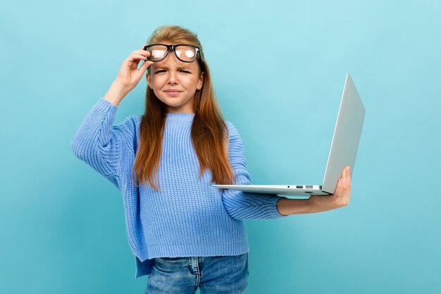 Attraktives europäisches Mädchen in den Gläsern mit einem Laptop in den Händen auf hellblauer Wand