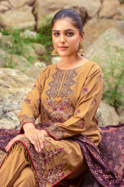 Attraktives junges Mädchen, das auf Felsen posiert und traditionelles Desi-Kleid für Modeaufnahmen im Freien trägt