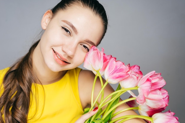 Attraktives junges Mädchen in einem gelben Kleid, das den Frühling genießt und duftende Blumen hält und lächelt