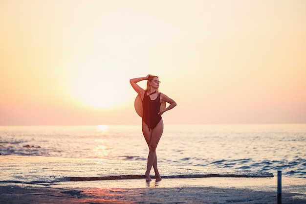 Attraktives junges Mädchen mit langen Haaren posiert vor der Kamera am Strand Sie trägt einen schwarzen Badeanzug Goldenes Sonnenuntergangslicht