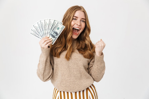 Attraktives junges Mädchen mit Pullover, das isoliert über weißer Wand steht, Geldbanknoten zeigt, feiert