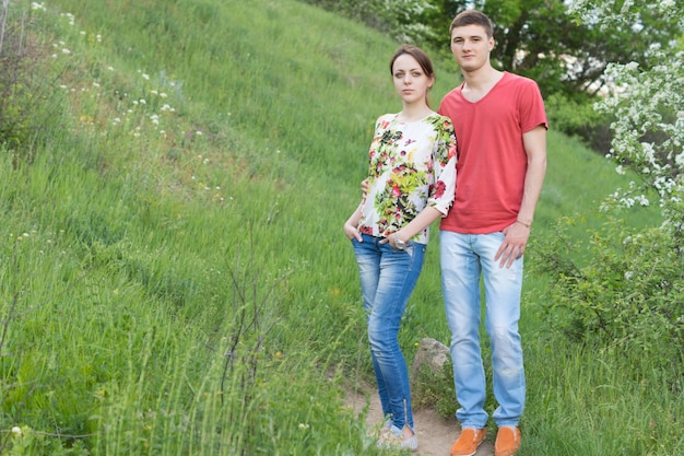 Attraktives junges Paar, das einen Tag in der Natur genießt, das nahe beieinander auf einem grasbewachsenen Hügel neben einem Baum in der Frühlingsblüte steht
