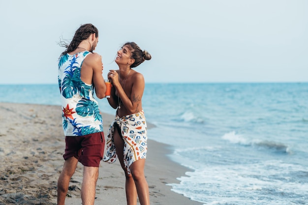 Attraktives junges Paar mit Alkoholcocktails, die am Strand spazieren gehen