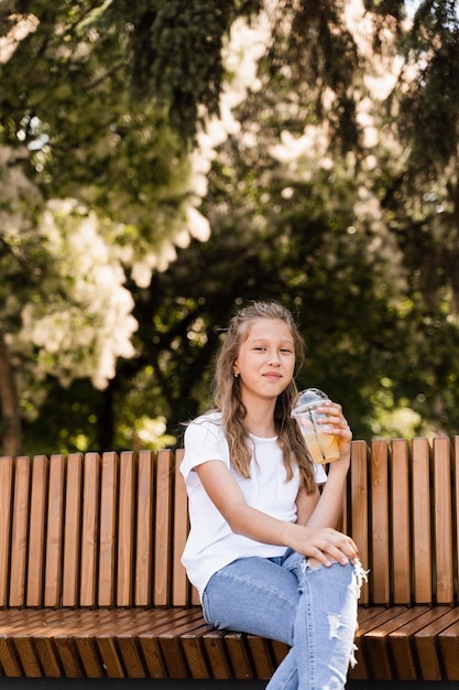 Attraktives Kindermädchen, das Sommerlimonade trinkt Sommercocktails Glückliches Mädchen, das Tasse mit Orangenlimonade im Freien hält