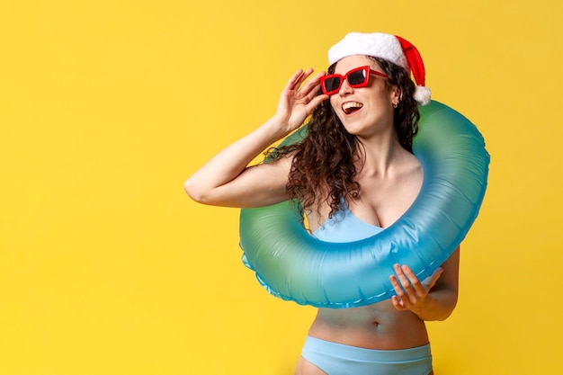 Attraktives Mädchen in Badeanzug und Sonnenbrille mit Weihnachtsmannshut und aufblasbarem Schwimmring lächelt