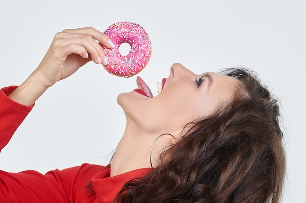 Attraktives Mädchen in einem roten Kleid leckt einen Donut