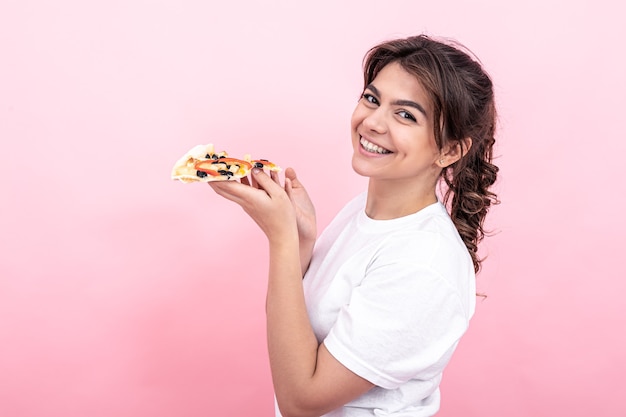 Attraktives Mädchen mit einem Stück Pizza auf einem rosa Hintergrundkopierraum