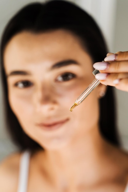 Foto attraktives mädchen mit einem tropfen ätherischen öls in einer pipette in den händen, nahaufnahme. junge frau trägt feuchtigkeitsspendendes serum auf ihre haut auf