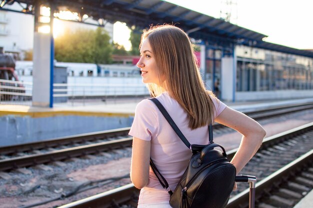 Attraktives Mädchen steht mit Gepäck am Bahnhof und wartet auf den Zug