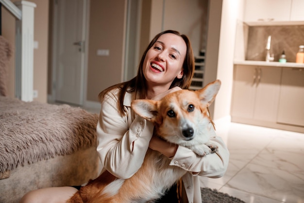 Attraktives Mädchen umarmt und spielt mit dem Corgi-Hund zu Hause Welsh Corgi Pembroke mit seiner Besitzerin auf dem Boden im Wohnzimmer