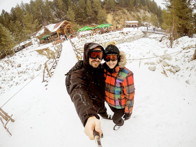 Attraktives Paar, das fantastisches Selfie mit einer mit Schnee bedeckten Holzhütte nimmt