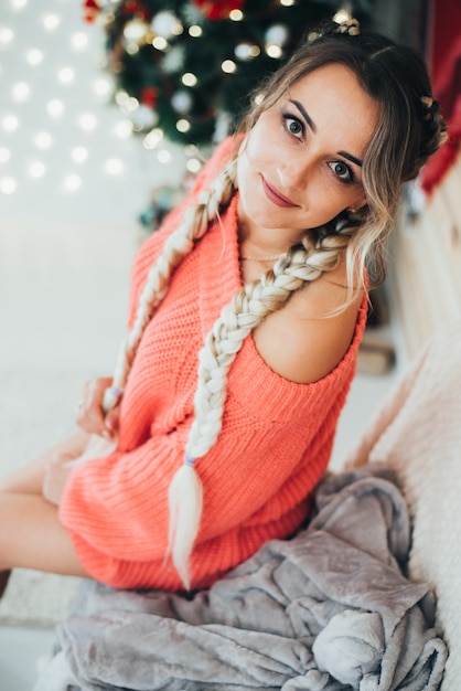 Attraktives schönes Mädchen mit zwei Boxer-Zöpfen, mit nackten Beinen in einem Pullover auf dem Hintergrund von Weihnachtsschmuck sexy