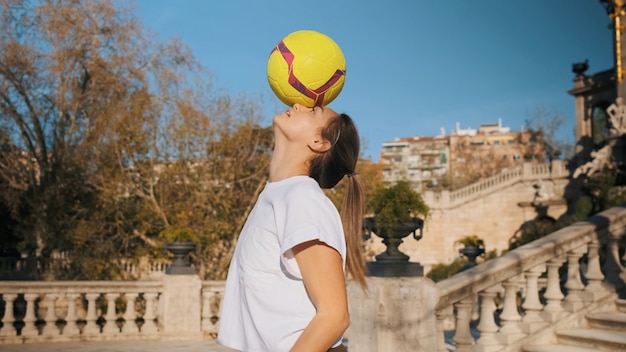 Attraktives sportliches Mädchen, das Fußballfähigkeiten im Stadtpark übt