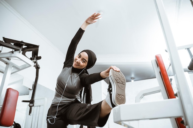 Foto attraktives sportliches muslimisches mädchen lächelt und schaut in die kamera, während sie ihren körper im fitnessstudio dehnt