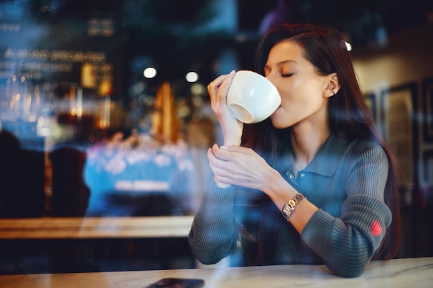 Attraktives süßes Mädchen, das Kaffee trinkt, während es in einem Café sitzt