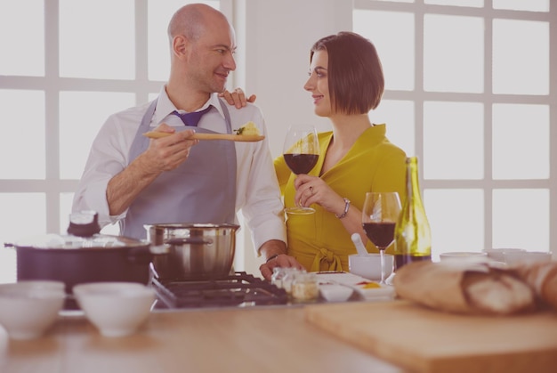 Attraktives verliebtes Paar kocht und öffnet den Wein in der Küche, während sie das Abendessen für einen romantischen Abend zubereiten