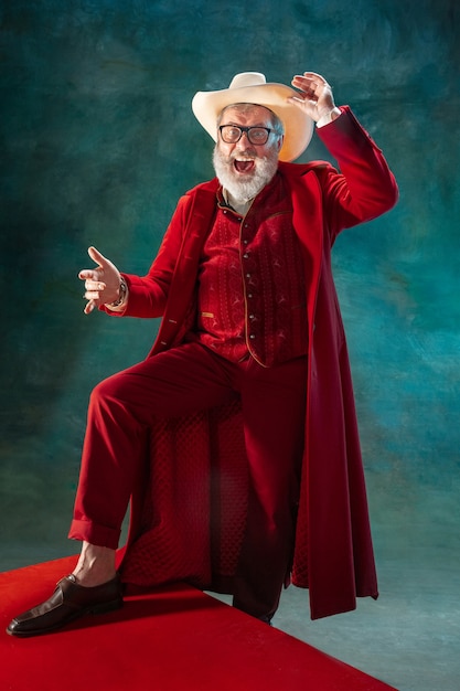 Atuando. homem moderno e elegante em um terno vermelho elegante e chapéu de cowboy em fundo escuro.