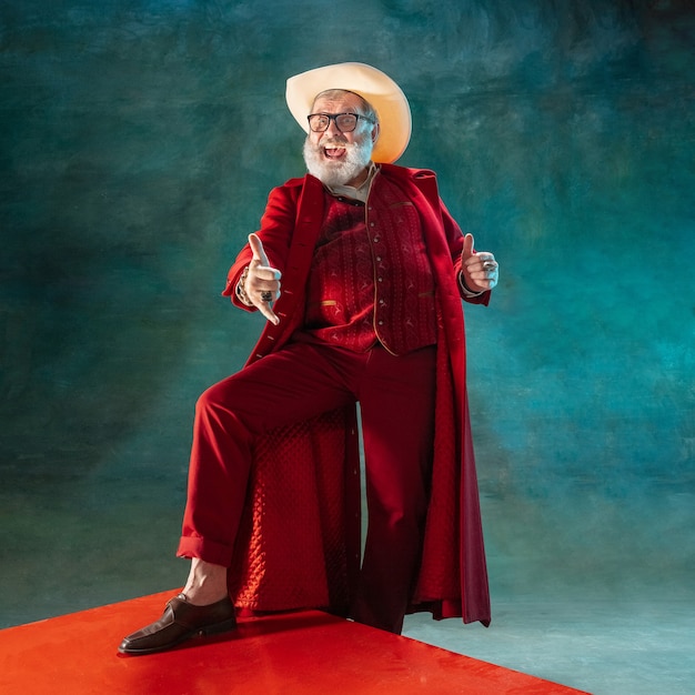 Atuando. Moderno e elegante Papai Noel em um terno vermelho elegante e chapéu de cowboy em fundo escuro. Parece uma estrela do rock. Reveillon e Natal, comemoração, feriados, clima de inverno, moda.