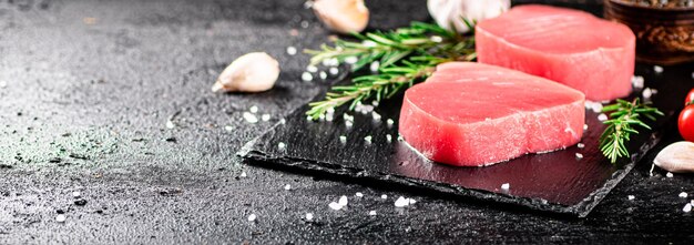 Foto atún crudo en una tabla de piedra con romero y ajo