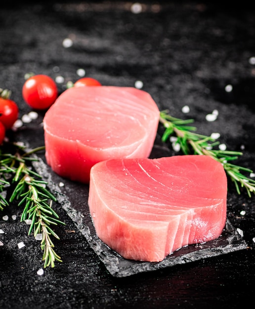 Atún crudo en una tabla de piedra con romero y tomates