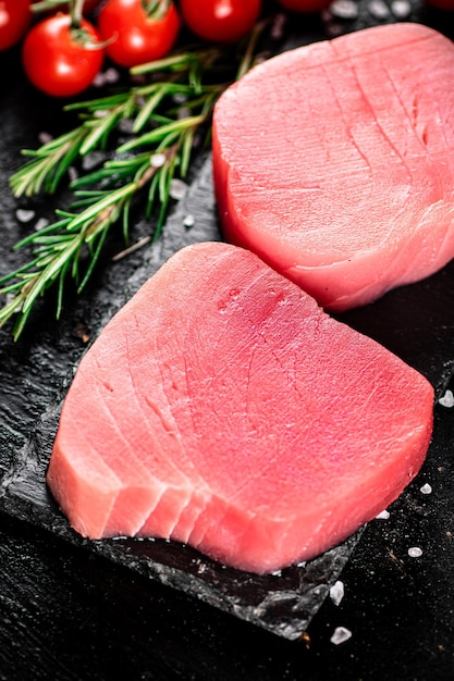 Atún crudo en una tabla de piedra con romero y tomates