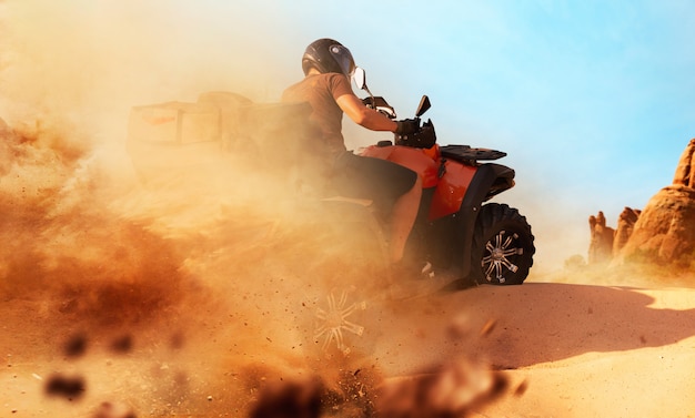 Atv andando em pedreira de areia, nuvens de poeira. Piloto masculino usando capacete em moto-quatro, freeriding extremo em moto-quatro nas dunas do deserto