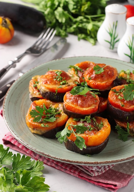 Auberginen und Tomaten gebacken mit Suluguni-Käse und Knoblauch, serviert auf einem Teller auf hellgrauem Hintergrund