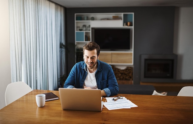 Auch zu Hause läuft alles wie gewohnt. Aufnahme eines hübschen jungen Geschäftsmannes, der sich hinsetzt und mit seinem Laptop einen Videoanruf entgegennimmt, während er von zu Hause aus arbeitet