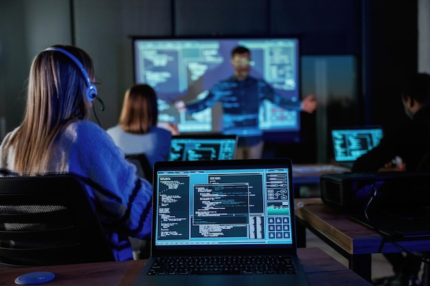 La audiencia está con las computadoras portátiles el entrenador de negocios masculino está en contra del proyector con datos enseñando a la gente