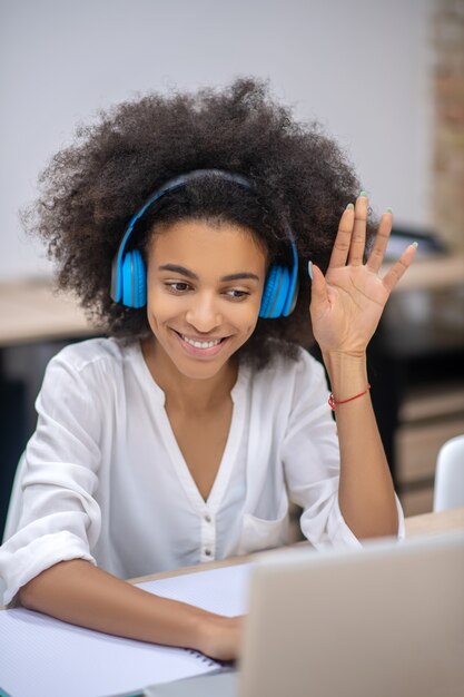 Audioanruf. Dunkelhäutiges hübsches Mädchen in Kopfhörern, das am Tisch sitzt