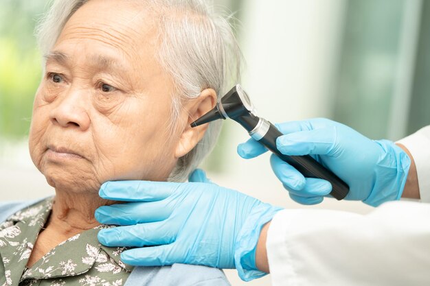 Foto audiologista ou médico otorrinolaringologista usa otoscópio para verificar a orelha de uma paciente asiática idosa que trata de problemas de perda auditiva