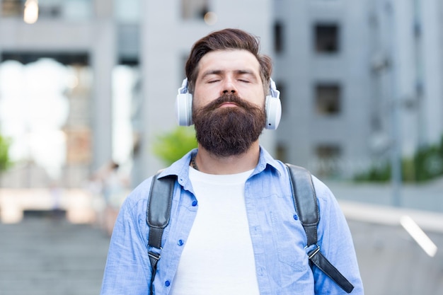 Audiomeditation Bärtiger Mann hört Musik mit geschlossenen Augen Hipster trägt Audiokopfhörer im Freien Entspannender Audiostream HiFi-Audiogerät Neue Technologie Modernes Leben Entspannen Zuhören Fühlen