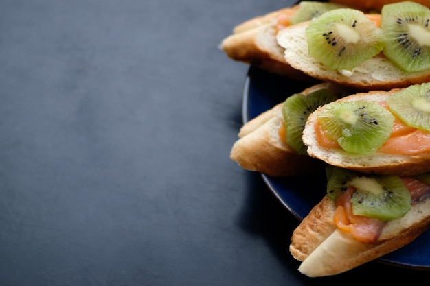 Auf blauem Teller liegen Sandwiches mit Baguette, Butter, Lachs und Kiwi