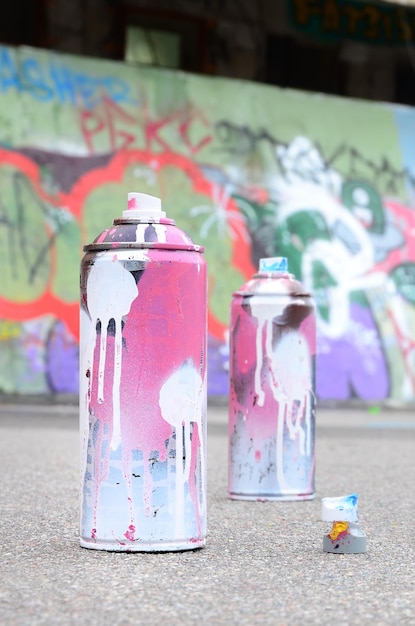 Foto auf dem asphalt neben der bemalten wand liegen in farbigen graffiti-zeichnungen mehrere gebrauchte sprühdosen mit rosa und weißer farbe und kappen zum sprühen von farbe unter druck