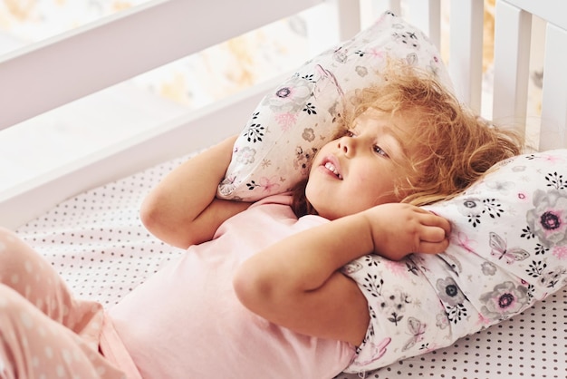 Auf dem Bett liegend Süßes kleines Mädchen in Freizeitkleidung ist tagsüber zu Hause