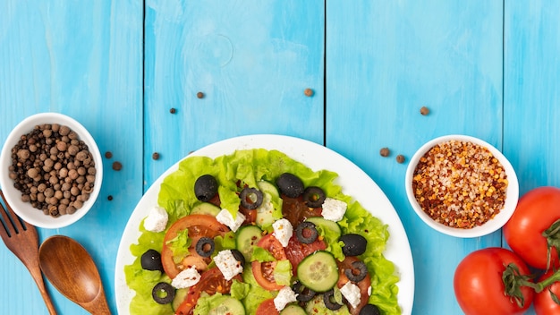 Auf dem blauen Holztisch steht ein Teller mit leckerem griechischem Salat.