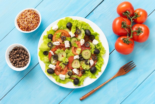 Auf dem blauen Holztisch steht ein Teller mit leckerem griechischem Salat.