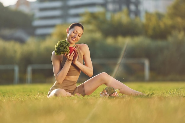 Auf dem Boden mit Gemüse Junge Frau in Yoga-Kleidung ist draußen auf dem Feld
