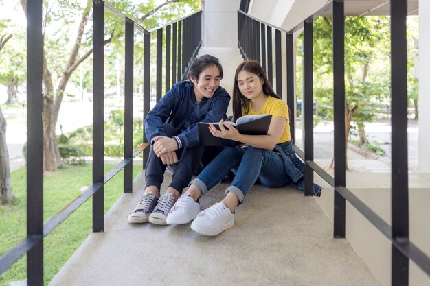 Auf dem Campus der Universität sitzen zwei asiatische Paare mit erhobenen Daumen im Treppenhaus und arbeiten an Laptops.