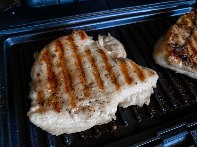 Auf dem Grill des Elektrogrills liegt ein Stück Hähnchensteak in Nahaufnahme mit schönen braun-goldenen Streifen aus den Grillaufsätzen. Gesundes Essen.